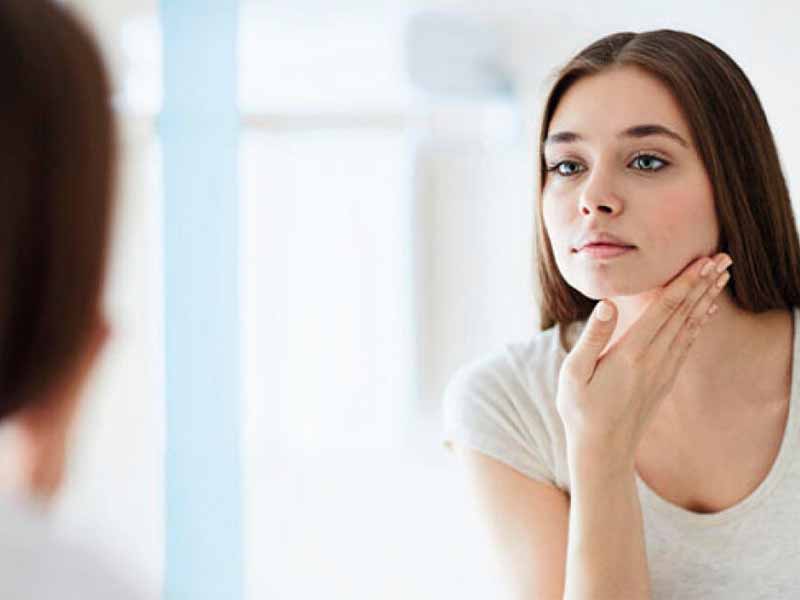 A woman examining her face in a mirror, illustrating the question of whether eczema is contagious.